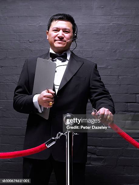 doorman opening rope barrier, smiling, portrait - doorman stockfoto's en -beelden