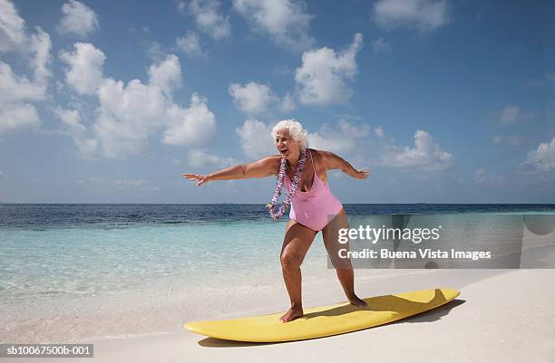 senior woman standing on surfboard - old woman in swimsuit stock-fotos und bilder