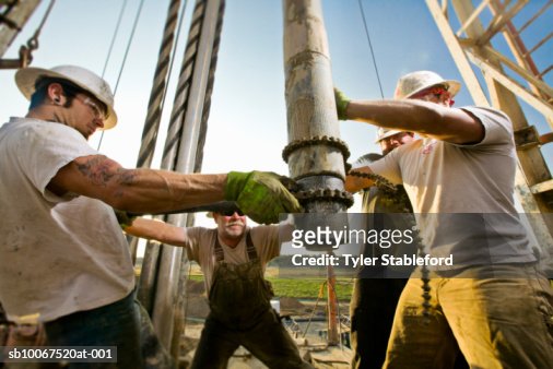 Oil workers using chain to position drill on drilling platform