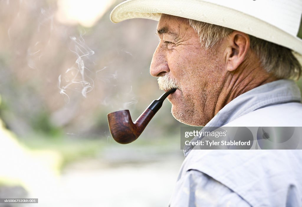 Mature man smoking pipe outdoors, profile