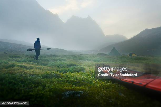 greenland, tasiilaq, man with kayak paddle walking in mist to camping tent - carrying kayak stock pictures, royalty-free photos & images