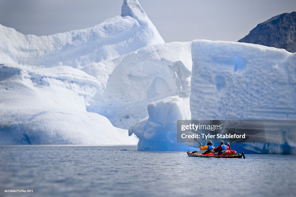 Greenland, Tasiilaq, two sea kayakers paddling below iceberg on Greenland Sea