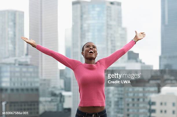 young woman with arms outstretched, cityscape in background - arms raised photos et images de collection