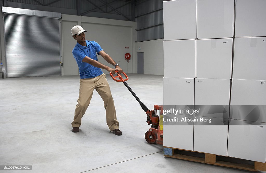 Male employee pulling pallet of boxes inside warehouse