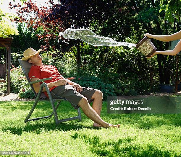 person throwing water out of bucket on man sleeping on deck chair in garden - throwing water stock pictures, royalty-free photos & images