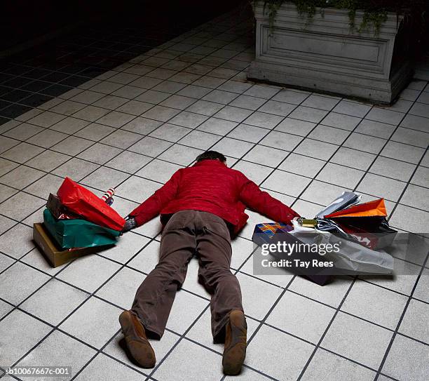 man holding shopping bags lying face down on floor, rear view - geld ausgeben stock-fotos und bilder