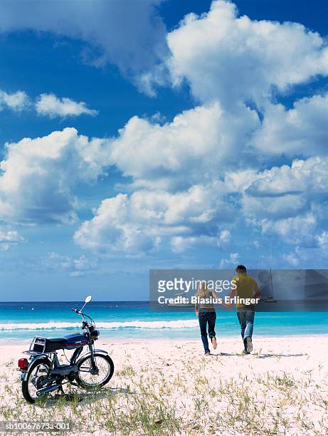 couple holding hands running towards ocean, motorbike in foreground, rear view - mare moto foto e immagini stock