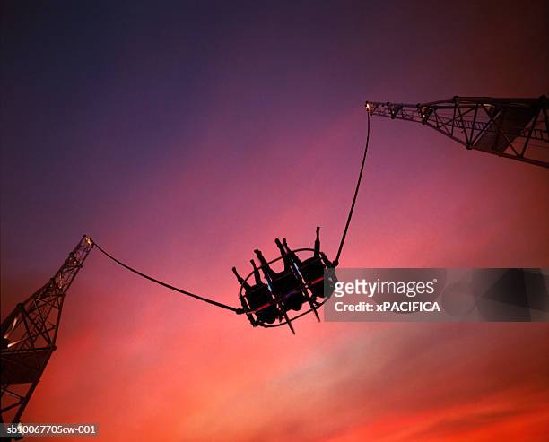 singapore, silhouettes of three people on bungee slingshot at sunset, directly below - bungee jump - fotografias e filmes do acervo
