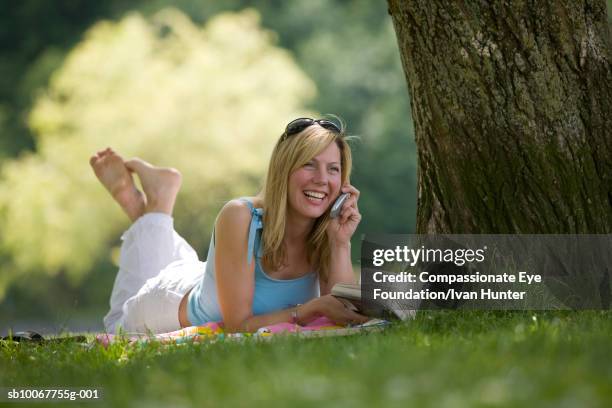 young woman lying on grass in park, talking on cell phone - donne bionde scalze foto e immagini stock