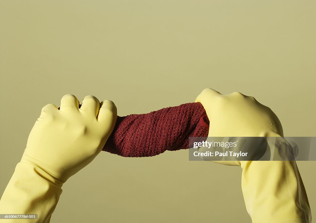 Person in rubber gloves wringing out towel, close-up of hands