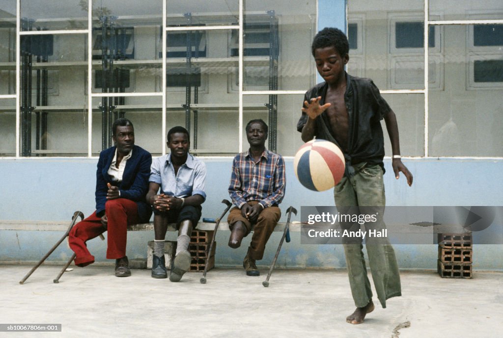 Angola, Huambo District, Artificial Limb Hospital, boy (10-11) playing basketball, men watching