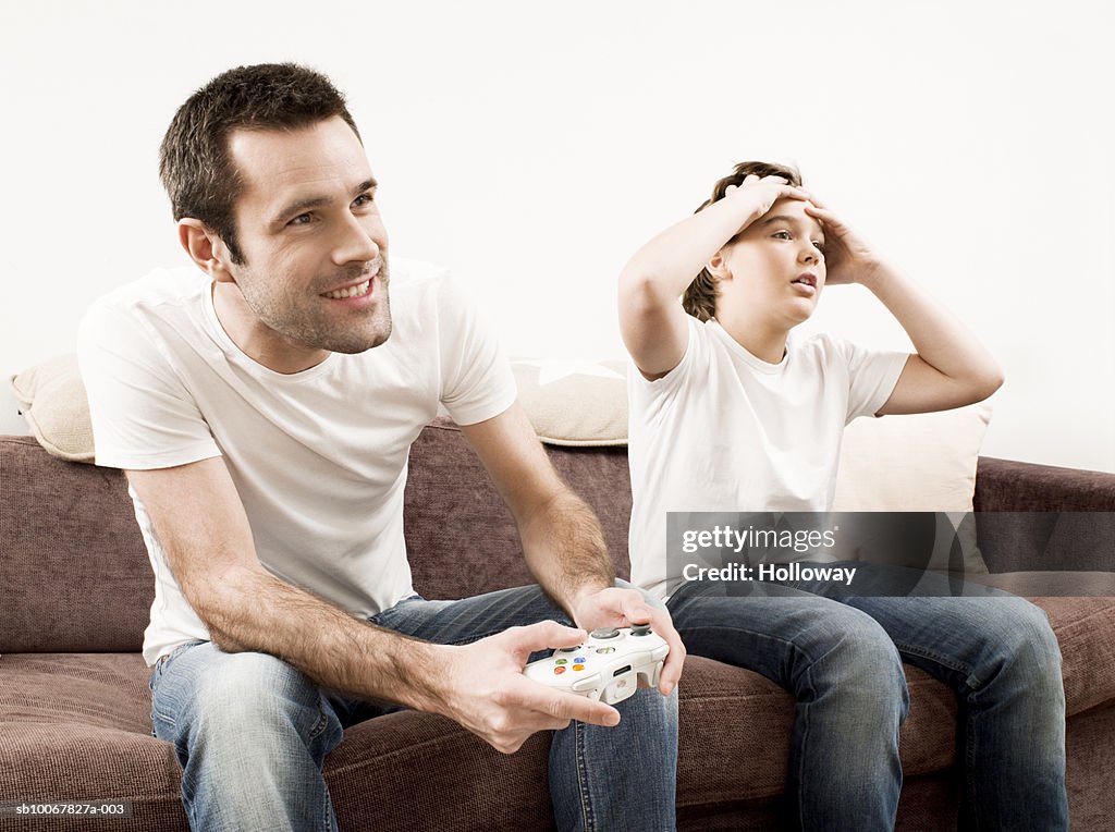 Father and son (10-11years) sitting sofa playing video games