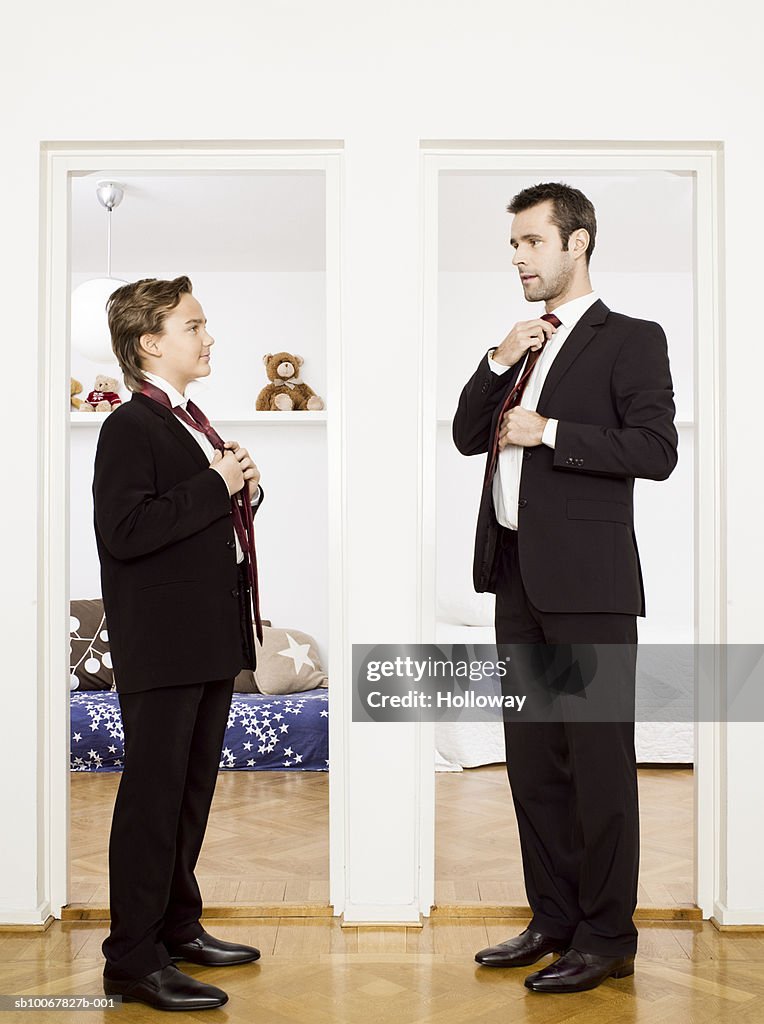 Father and son (10-11) putting on ties, standing face to face at home, side view