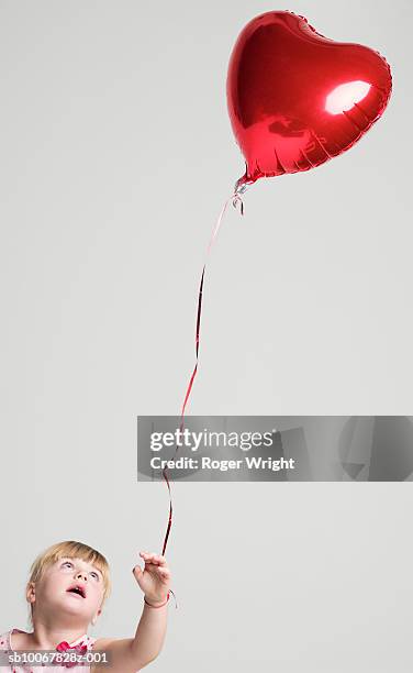 girl (2-3 years) with heart shaped balloon tied to hand, studio shot - child balloon studio photos et images de collection