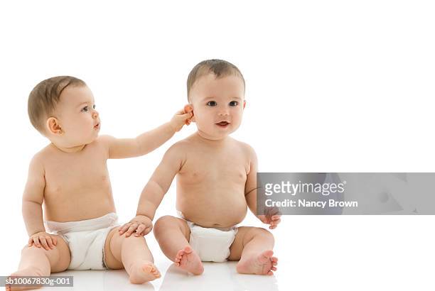 two baby boys (6-11 months) sitting on white background - pulling ear stock pictures, royalty-free photos & images