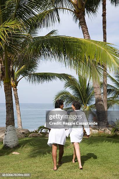 mature couple in bathrobes walking towards sea in bathrobes, rear view - robe stock pictures, royalty-free photos & images