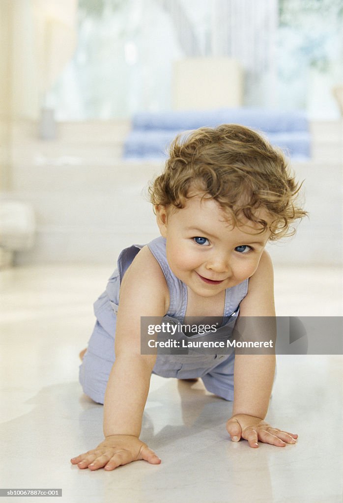 Baby boy (9-12 months) crawling on floor, smiling, portrait