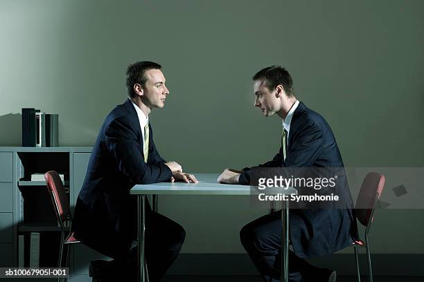 businessman looking at duplicate sitting at table in office (digital composite) - diverbio foto e immagini stock