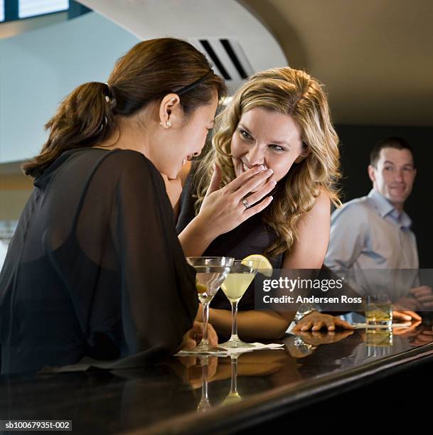 two women talking at bar counter, man in background watching - 3 liga fotografías e imágenes de stock