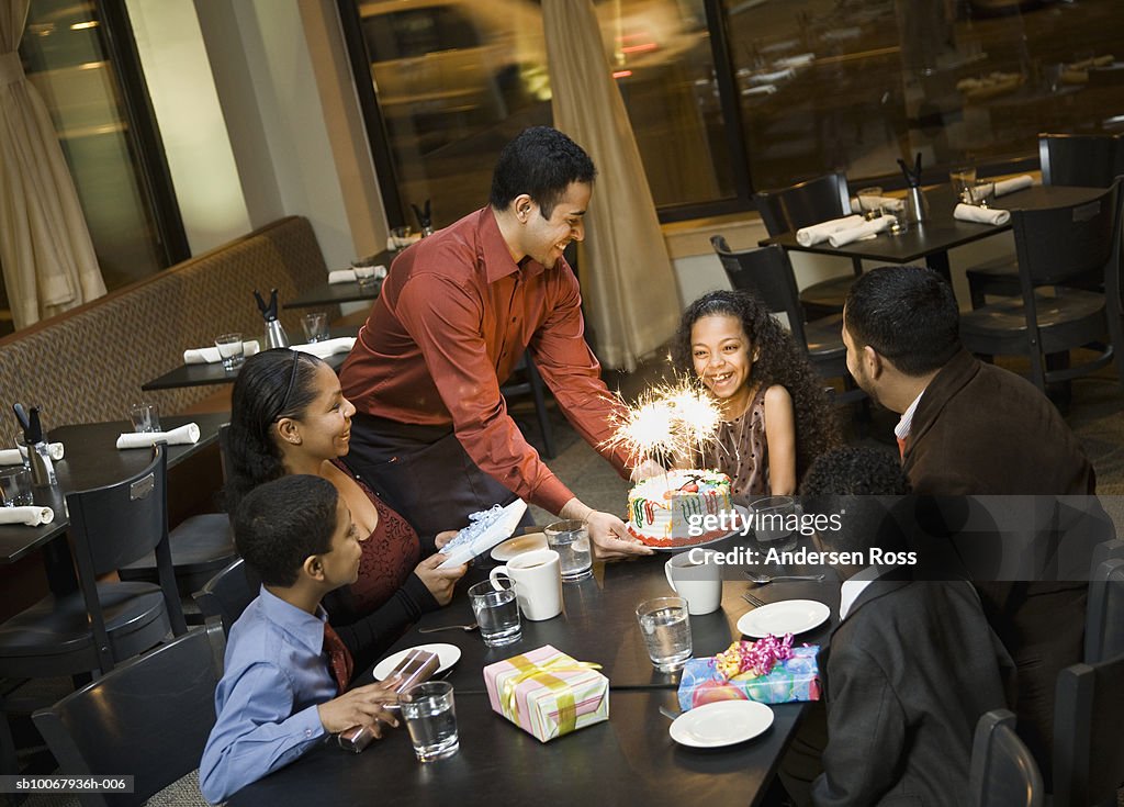 Waiter brings birthday cake for girl (10-11) during dinner