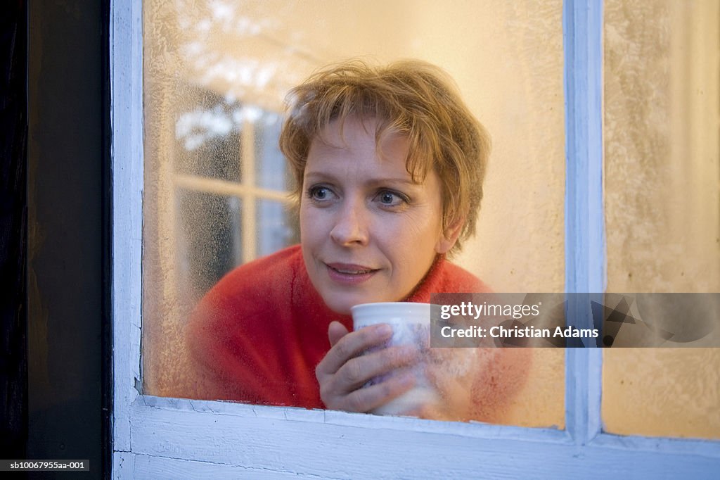 Mature woman holding coffee cup, looking out of window