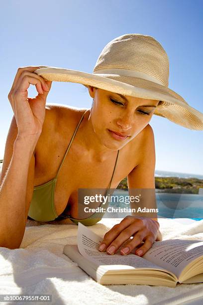 young woman lying at poolside, reading book - decolleté stockfoto's en -beelden