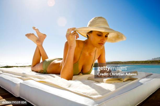 young woman lying at poolside, reading book - decolleté stockfoto's en -beelden