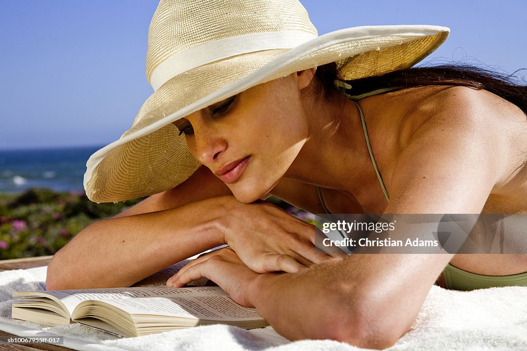 Young woman lying at poolside, reading book, close-up