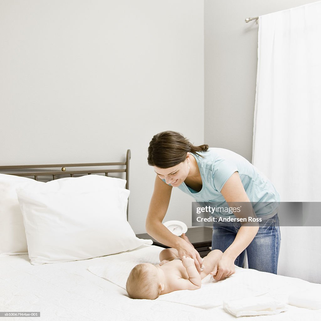 Mother changing baby's (8 months) clothes on bed