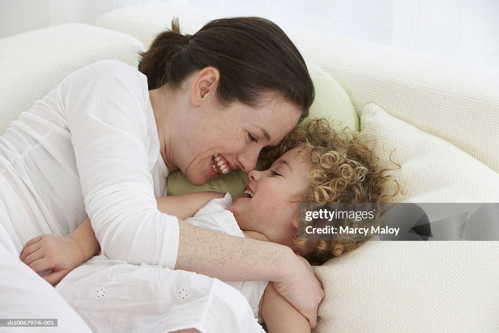 Mother and daughter (4-5 years) cuddling on sofa