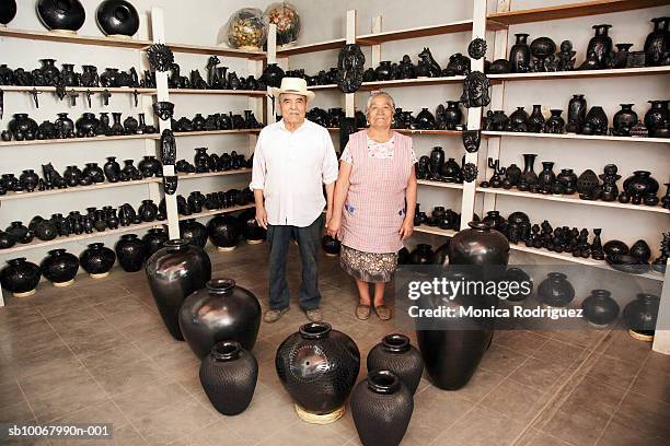 mexico, oaxaca, senior couple standing in pottery shop, portrait - artesanias mexicanas fotografías e imágenes de stock