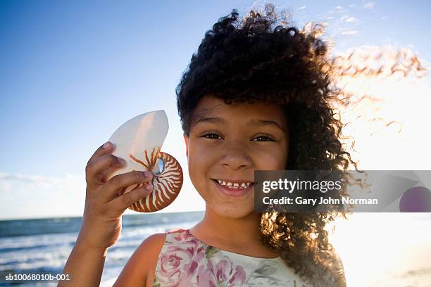 girl (6-7) holding shell to ear on beach, portrait, close-up - beach shells stock pictures, royalty-free photos & images