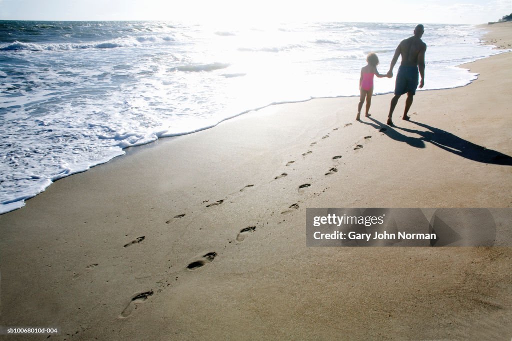 Father and daughter (6-7) walking on beach, rear view