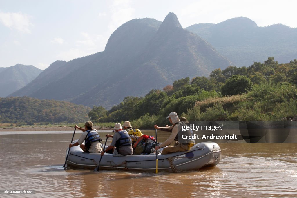 Tourists whitewater rafting in river, mountains in background