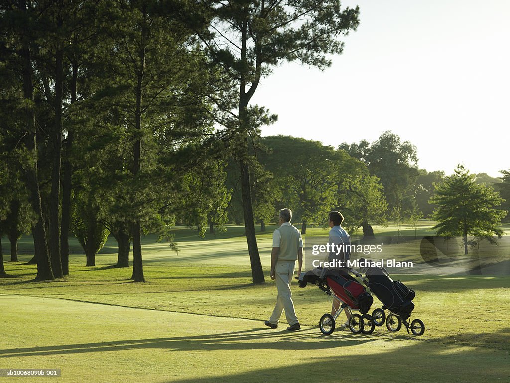 Two men pulling golf trolleys on course