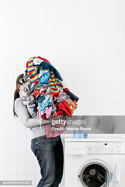 woman carrying large pile of laundry to washing machine - pile of clothes stock pictures, royalty-free photos & images