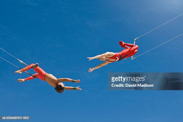 trapeze artists swinging towards one another, low angle view - trapéziste photos et images de collection