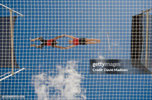 male trapeze artist catching man, low angle view - sicherheitsnetz stock-fotos und bilder
