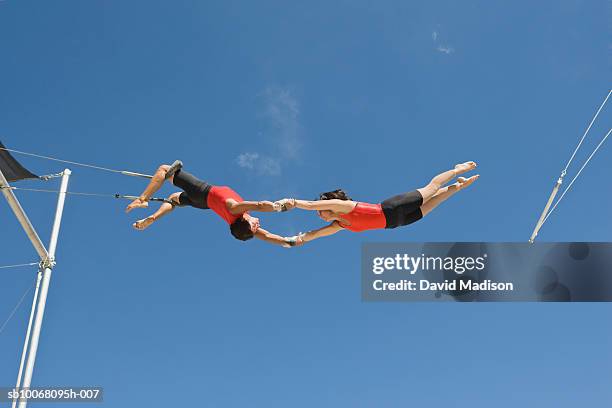 male trapeze artist catching woman, low angle view - trapezstange stock-fotos und bilder