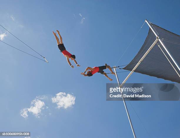 male trapeze artist catching man, low angle view - caught in the act stock-fotos und bilder