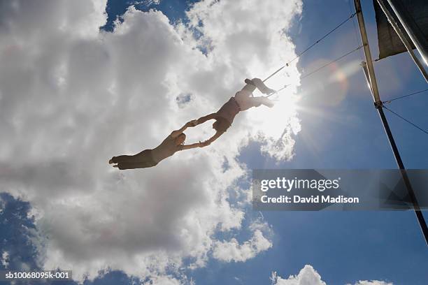 male trapeze artist catching woman, low angle view - trapezista foto e immagini stock