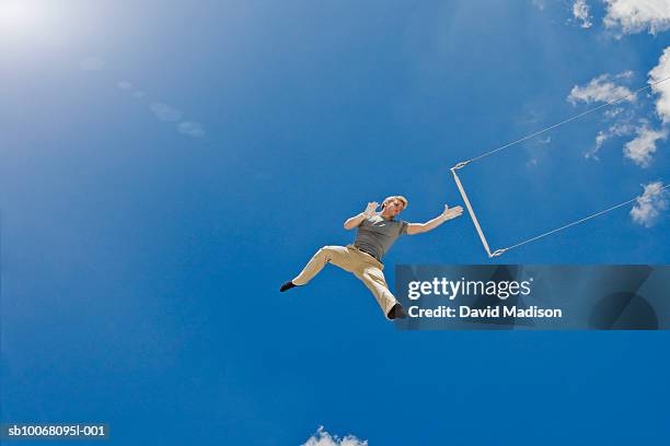 male trapeze artist performing on trapeze, low angle view - trapeze stock-fotos und bilder