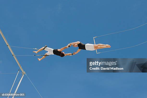 male trapeze artist catching man, low angle view - trapeze stock-fotos und bilder