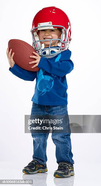 boy (2-3) wearing football helmet and holding football, studio portrait - american football ball studio stock pictures, royalty-free photos & images