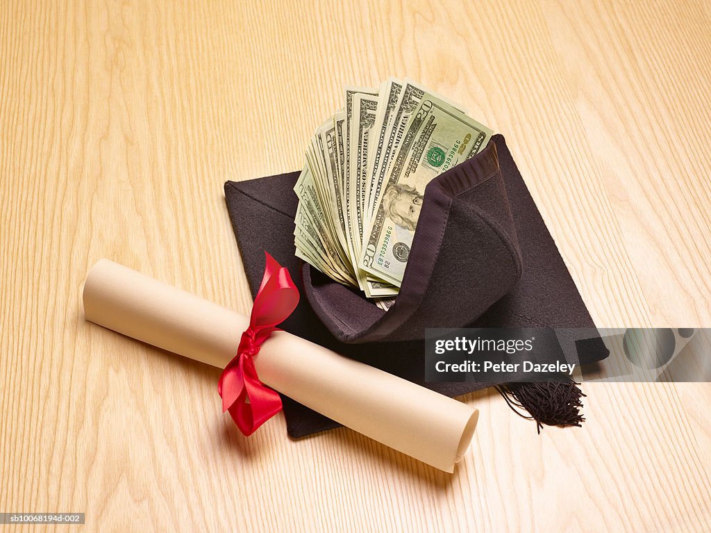 Rolled diploma and mortar board with US banknotes inside, studio shot