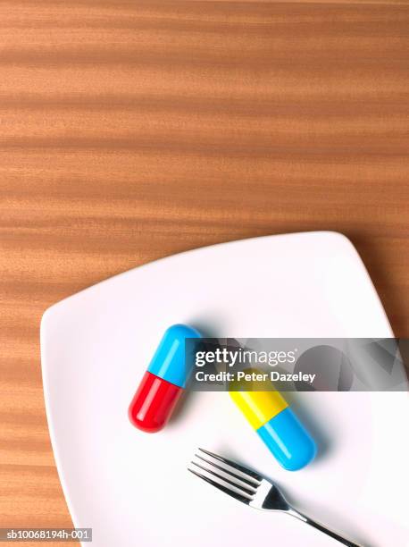 two capsules on plate with fork, studio shot, directly above - suplement stock pictures, royalty-free photos & images