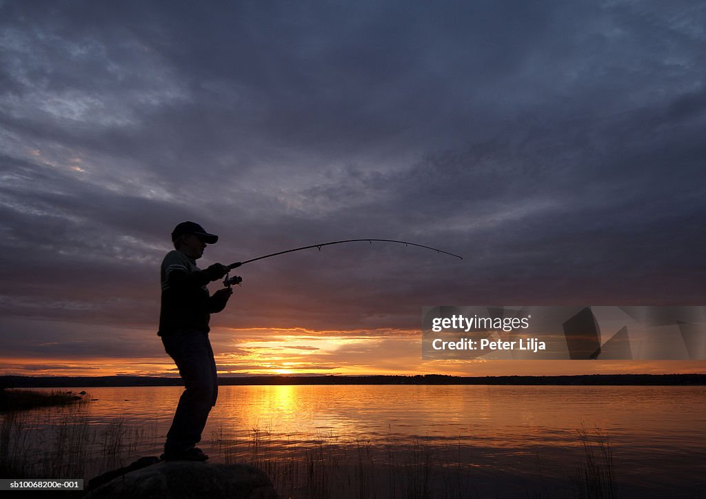 Silhouette Of Boy Fishing At Dusk Side View High-Res Stock Photo