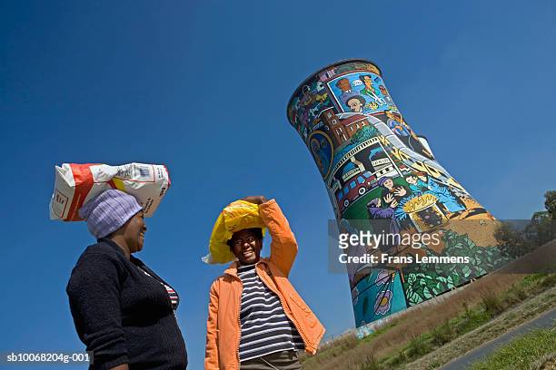 south africa, johannesburg, soweto two women chatting in front of orlando power station tower - soweto towers stock pictures, royalty-free photos & images