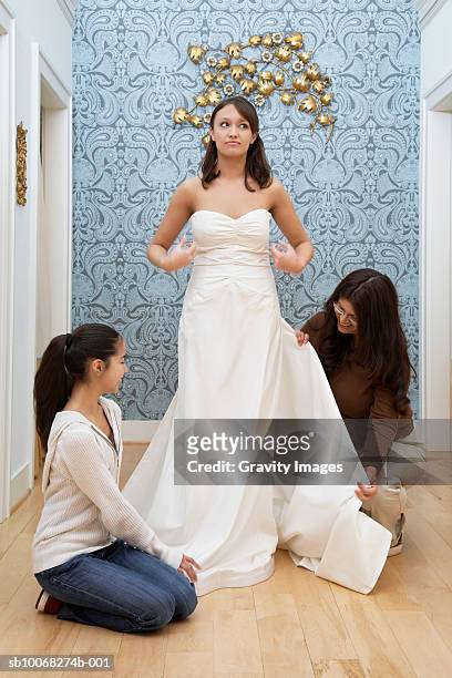 woman trying on wedding dress, mother and sister helping - girl changing room shop stock-fotos und bilder