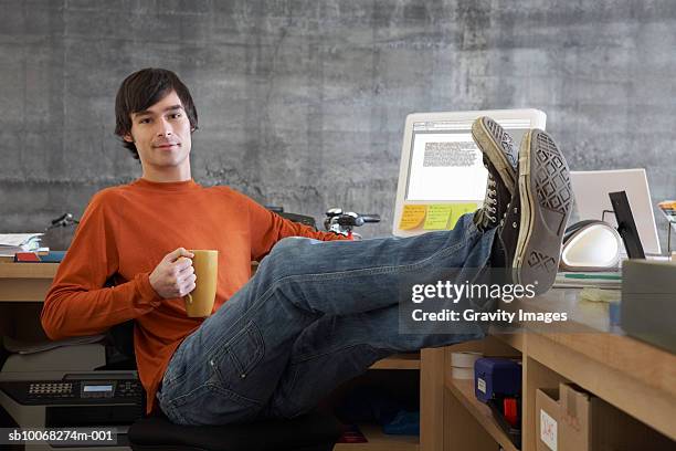 shop owner relaxing at desk holding mug, feet up, portrait - 足首を重ねる ストックフォトと画像